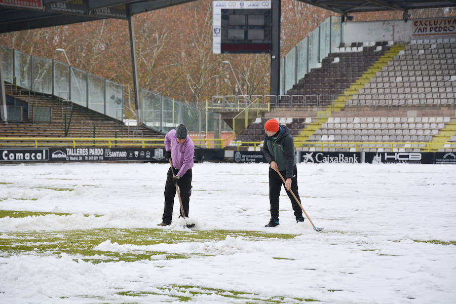 Operarios del servicio de mantenimiento del campo y voluntarios se afanan en retirar la nieve y el hielo del terreno de juego de El Plantío antes del Burgos CF - Barakaldo.