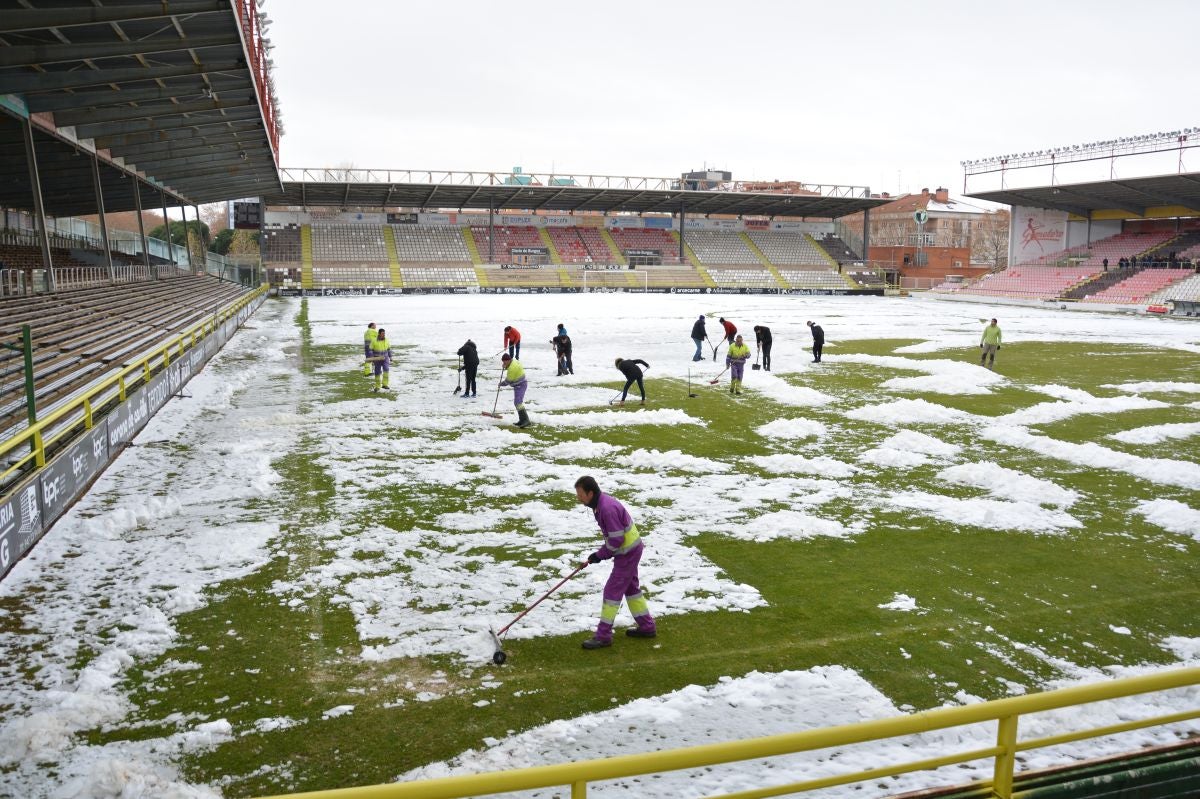 Operarios del servicio de mantenimiento del campo y voluntarios se afanan en retirar la nieve y el hielo del terreno de juego de El Plantío antes del Burgos CF - Barakaldo.