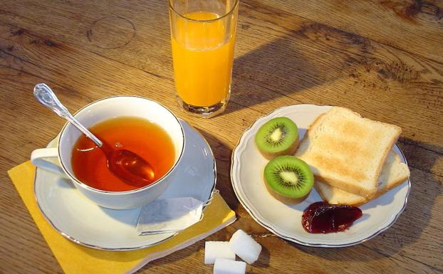 Desayuno a base de zumo, kiwi, mermelada, tostadas y una taza de té. 