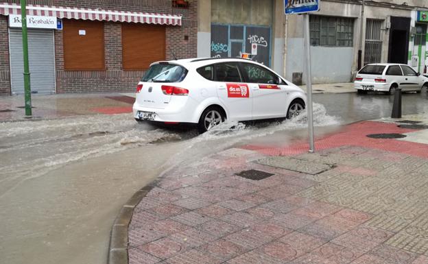 Un taxi cruza una balsa de agua en la calle Abad Maluenda.