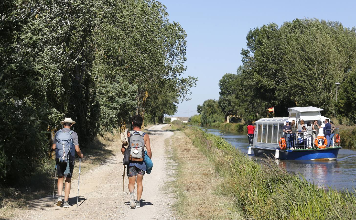 Dos peregrinos del Camino de Santiago se cruzan con el barco Juan de Homar en el Canal de Castilla entre Frómista y Boadilla del Camino (Palencia).