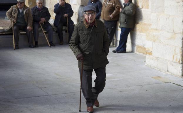 Un señor pasea por una plaza de Zamora ante un grupo de mayores reunidos en la misma zona. 