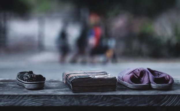 Unos zapatos abandonados que pertenecían a unos niños emigrantes venezolanos reposan junto a una vieja Biblia en un albergue de paso situado en el sector Guaduales de la carretera Cúcuta - Pamplona. Al fondo de la imagen un grupo de emigrantes venezolanos caminan rumbo a Bogotá.