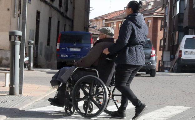 Una mujer ayuda a un jubilado en silla de ruedas a cruzar un paso de cebra en Segovia-