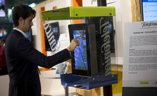 Un usuario carga su teléfono móvil a través de las nuevas cabinas mientras hace una consulta en la pantalla durante el Smart City Expo World Congress de Barcelona.