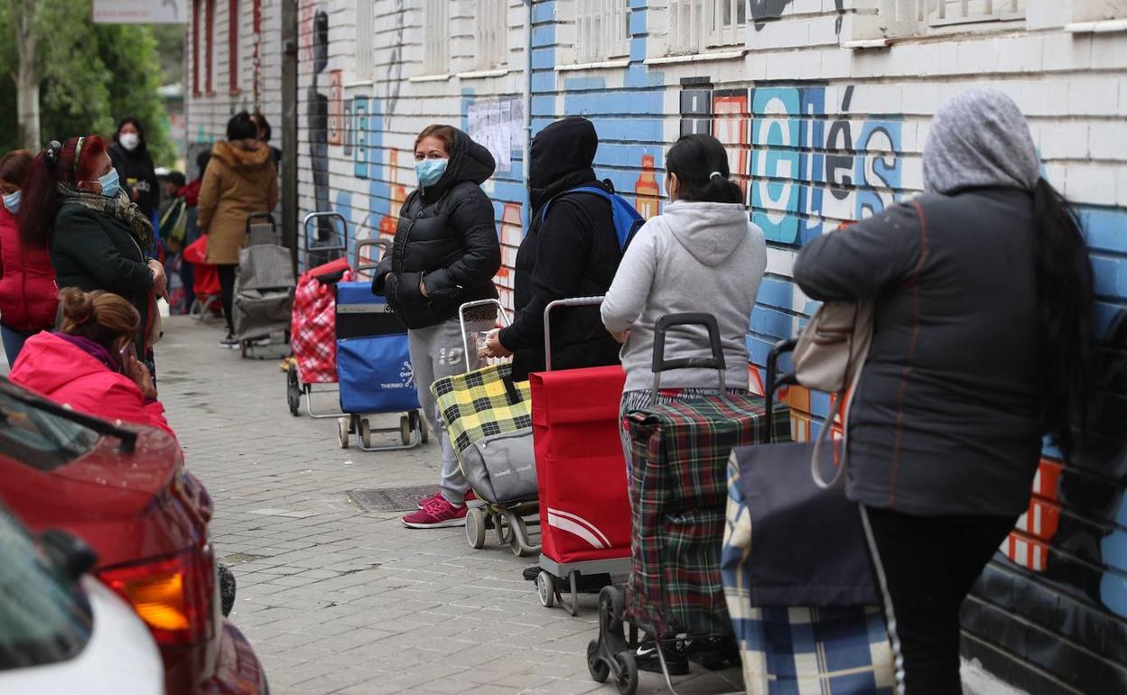 Varias personas esperan en la fila para recoger alimentos proporcionados por la Asociación de vecinos de Aluche, en Madrid.