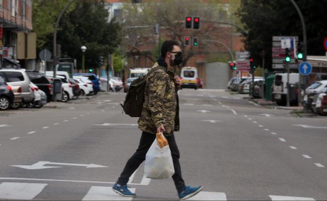 Un joven lleva la compra por una calle desierta por el estado de alarma, en Valladolid.