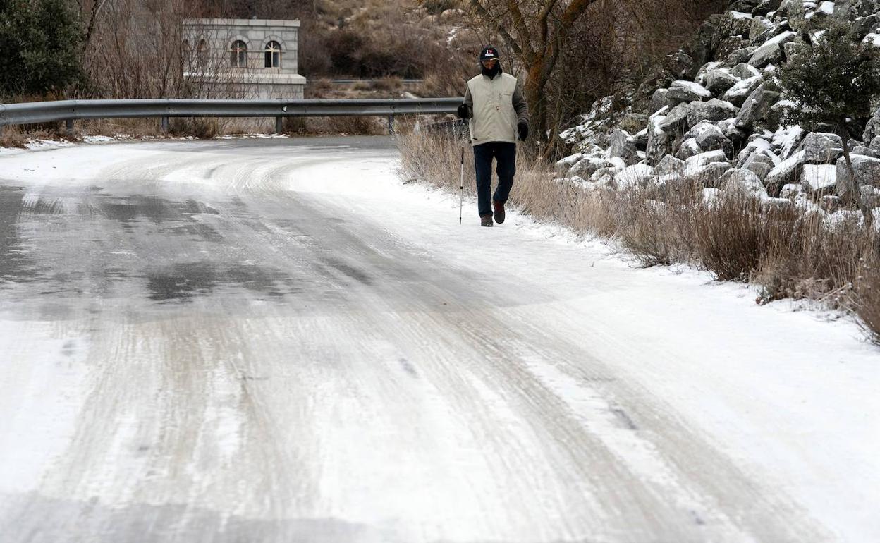 Un hombre pasea por un tramo de la carretera de acceso al embalse abulense de Fuentes Claras con placas de hielo.