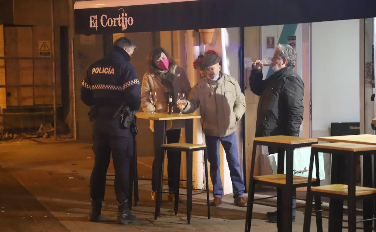 Un agente de la Policía Local informa a tres clientes del toque de queda a las 20:00 horas.