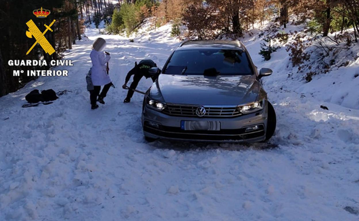 El agente de la Guardia Civil intenta liberar al vehículo de la nieve y el hielo.