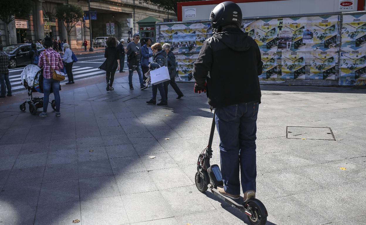 Una persona circulando con patinete electico por la acera.