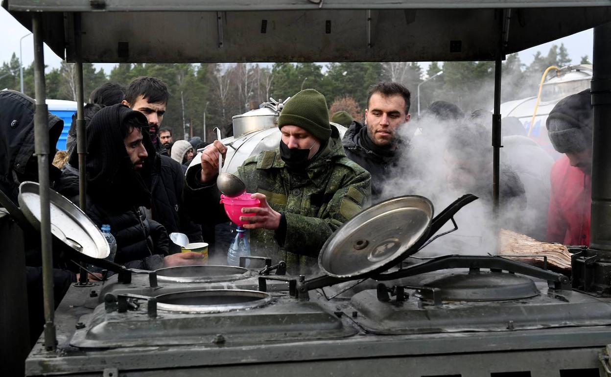 Inmigrantes en la frontera entre Bielorrusia y Polonia ante una cocina de campaña para recoger alimentos.