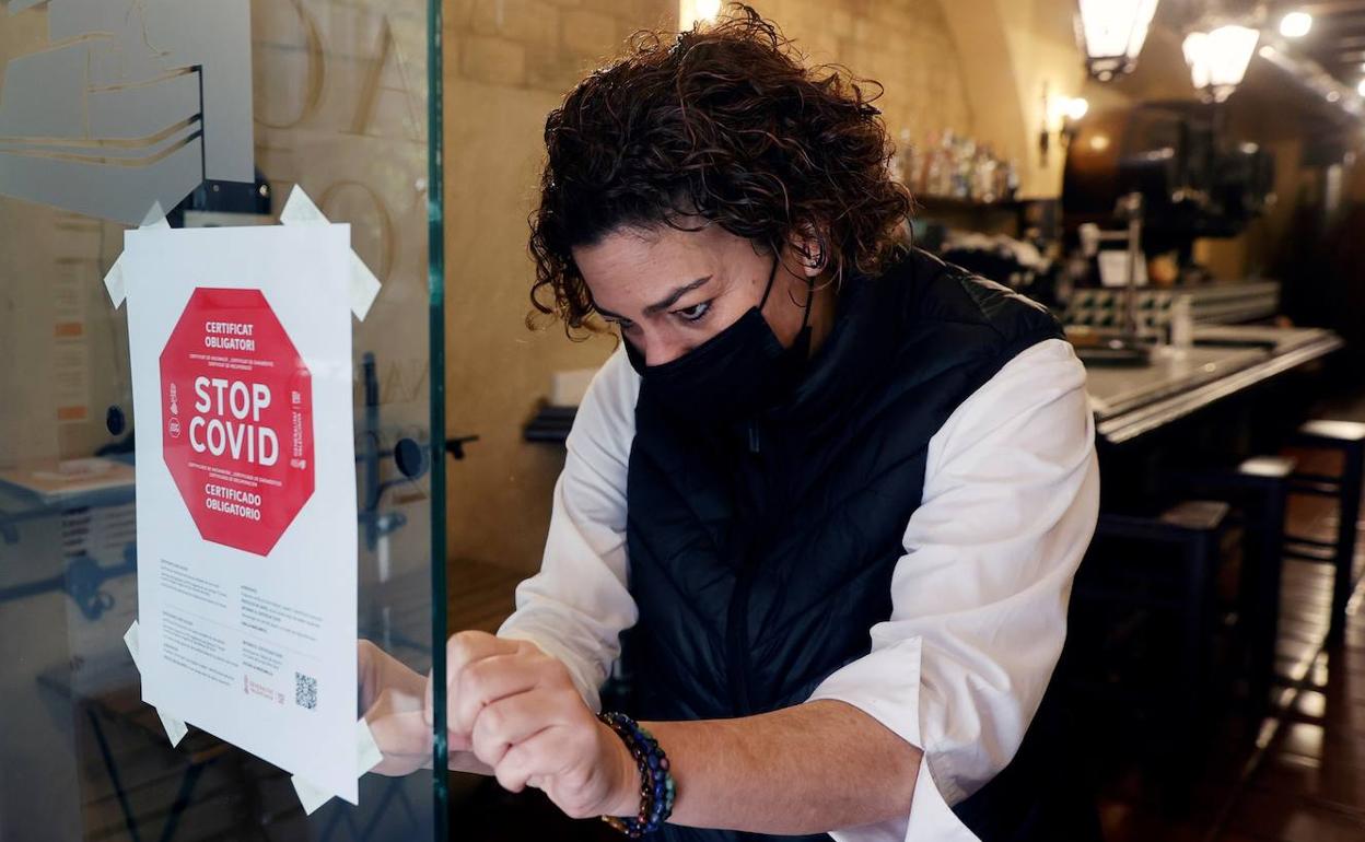 Una trabajadora coloca a la entrada de un restaurante la obligatoriedad de llevar el pasaporte covid. 