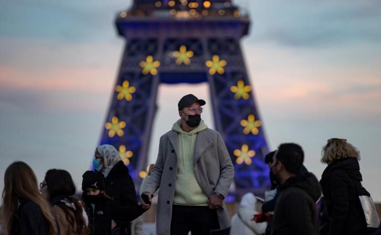 Un hombre con mascarilla, delante de la Torre Eifel. 