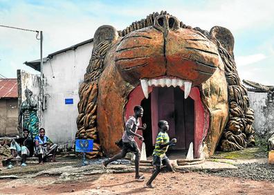 Imagen secundaria 1 - 1- El reino de la superstición. Un fetiche despliega sus artes en un arrabal paupérrimo de Porto Novo, capital de Benín. 2- Realismo mágico. Niños juegan ante la fachada de una casa que reproduce las fauces de un león en Savalou 3-Escenario de pesadilla. El sacerdote del Templo de las Pitones luce escarificaciones que simulan mordeduras