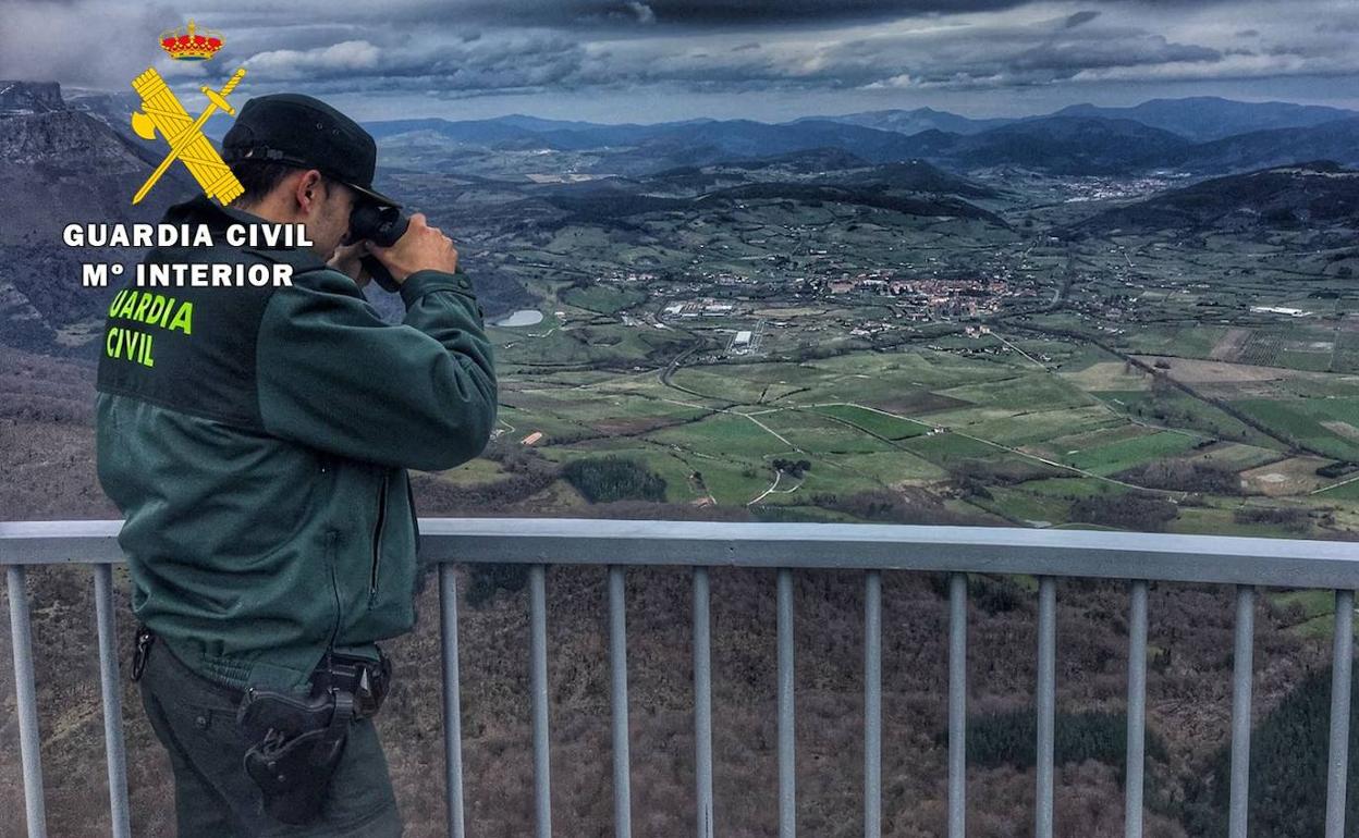 Un guardia civl otea el monte desde lo alto con unos prismáticos