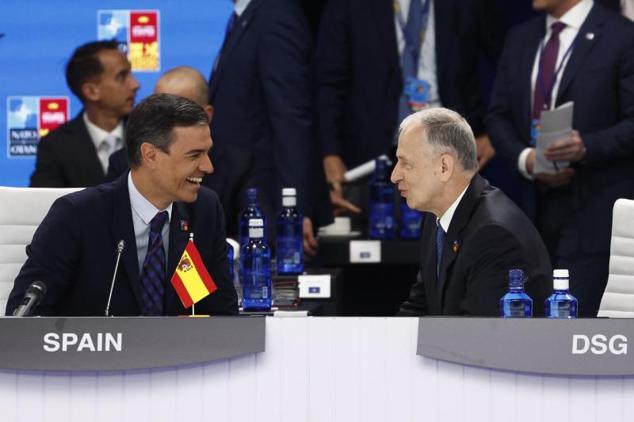 Sánchez conversa con un alto cargo de la OTAN. La bandera de España se encuentra al revés. 