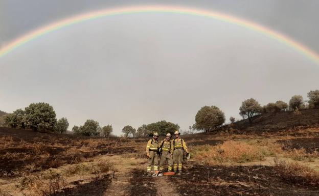 Tres bomberos de la BRIF La Iglesuela posan junto al terreno quemado debajo de un arcoiris