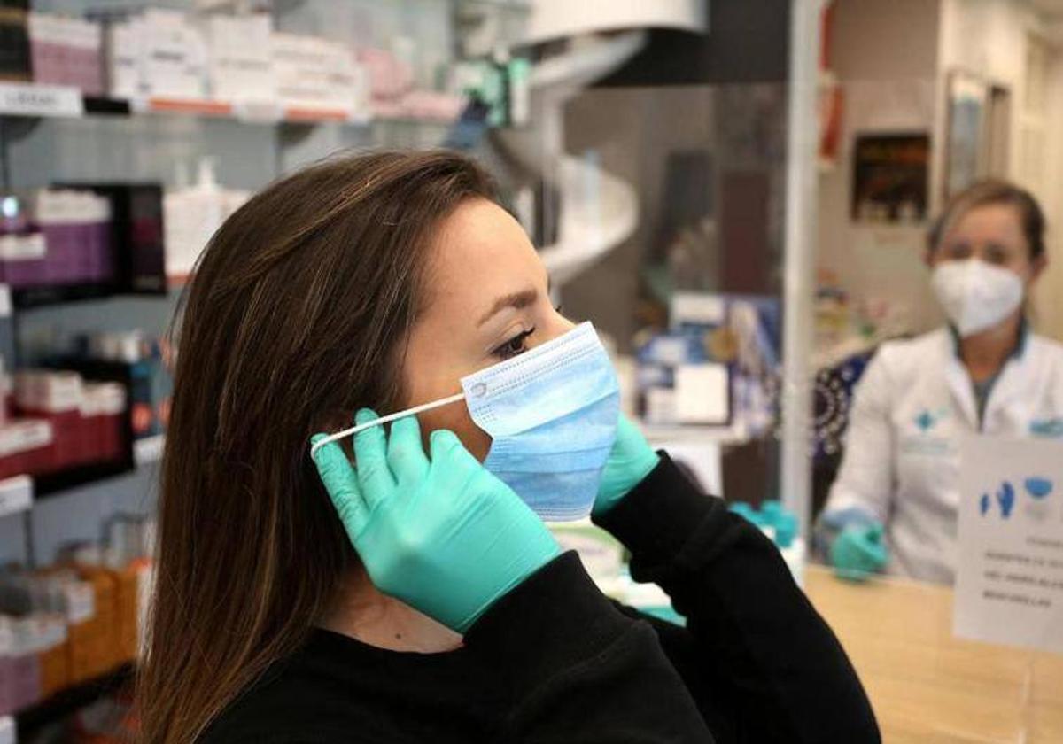 Una mujer se pone una mascarilla en una farmacia.