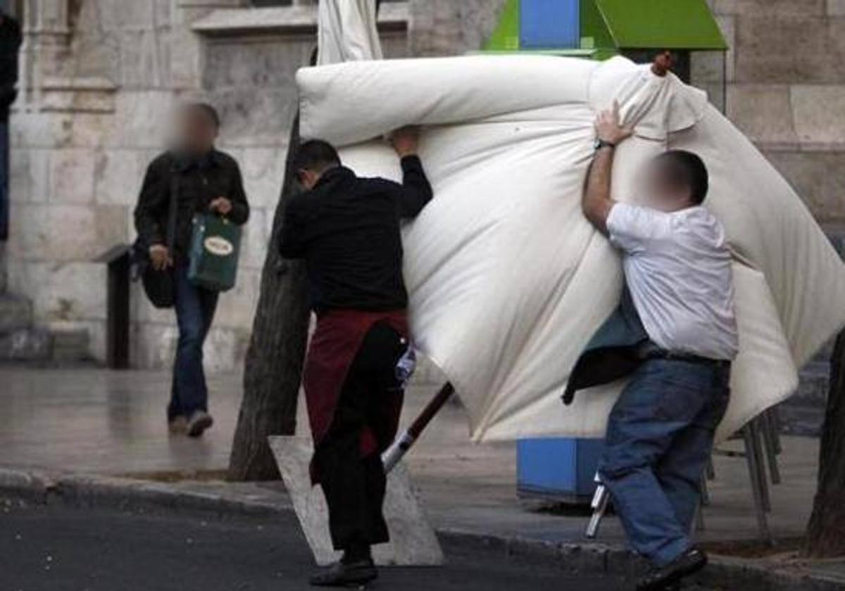 Dos trabajadores luchan contra el viento para recoger una sombrilla en Burgos.