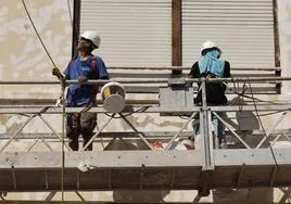 Dos trabajadores subidos a un andamio pintando la fachada de un edificio