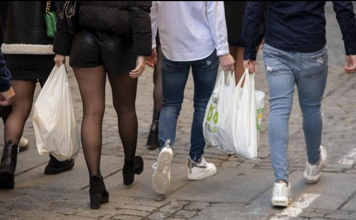 Chicos y chicas cruzan la calle con bolsas de botellas en la mano.