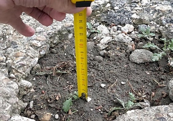 Un vecino indica la profundidad de los baches de las calles de la urbanización.