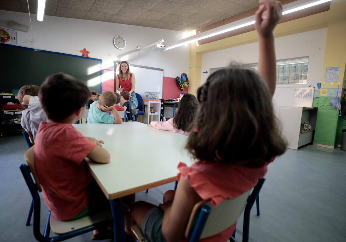 Una niña levanta la mano para llamar la atención de la profesora.