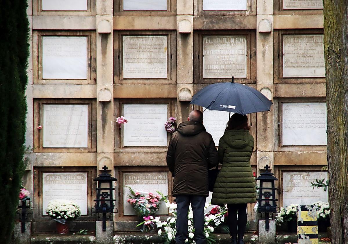 Dos personas frente a los nichos con flores en el cementerio de Burgos.