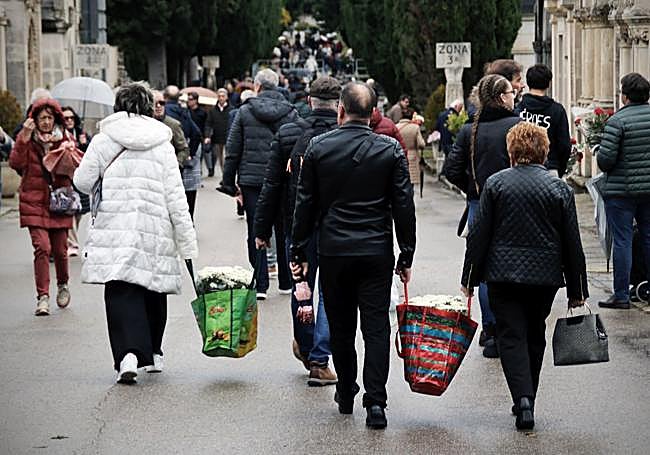 Varias personas se ayudan para llevar las flores en el cementerio de Burgos.