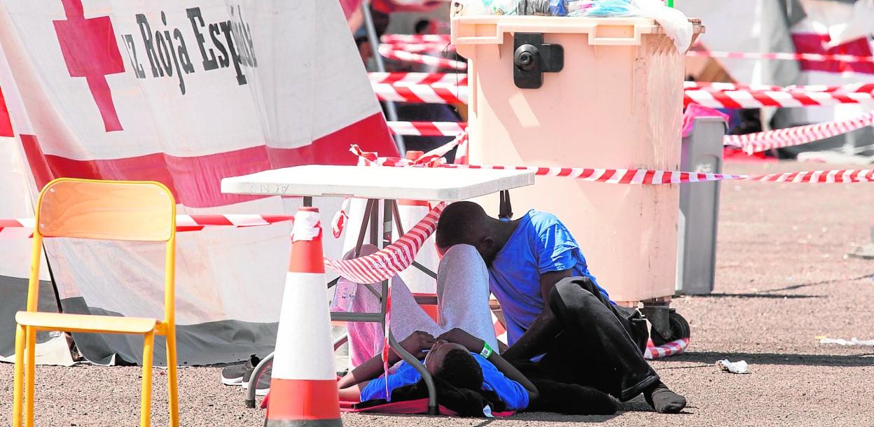 Dos inmigrantes de protegen del sol bajo una mesa en el muelle de Arguineguín, en una imagen tomada el pasado viernes. 