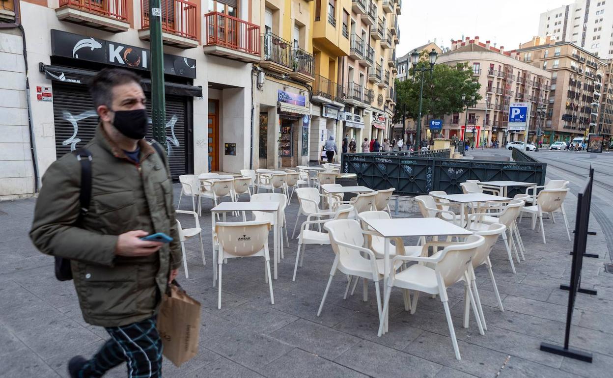 Un hombre camina junto a una terraza vacía en Zaragoza. 