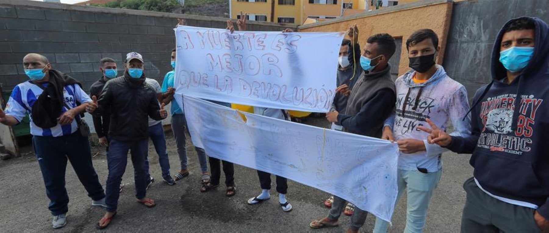 Varios jóvenes sostienen pancartas a las puertas del campamento del barrio El Lasso en una protesta celebrada en la jornada de este lunes. 