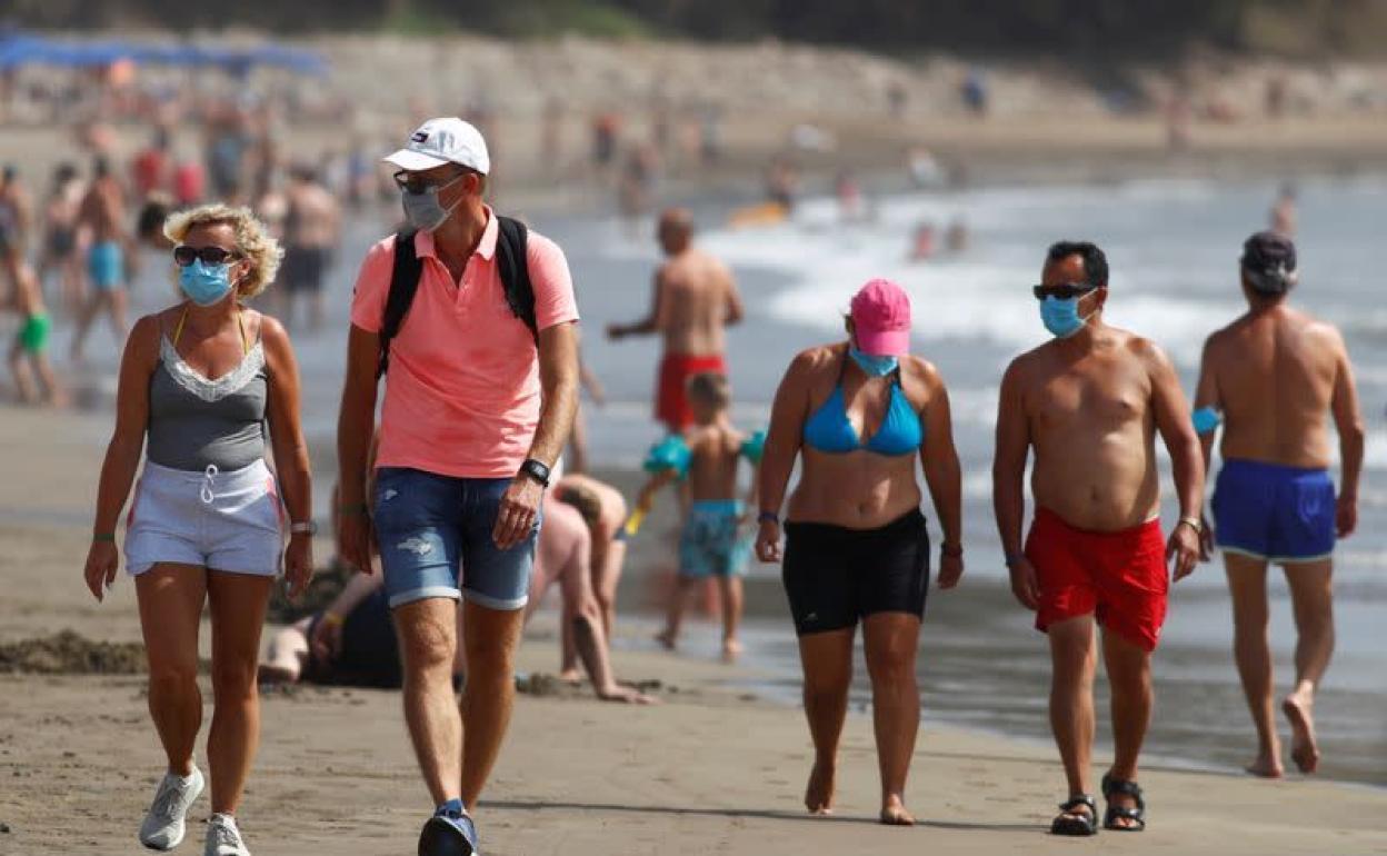 Varias personas caminan por la playa con mascarilla en Playa del Inglés, Gran Canaria. 
