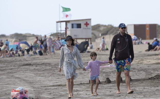 Imagen de una familia paseando abrigada por Playa del Inglés. 