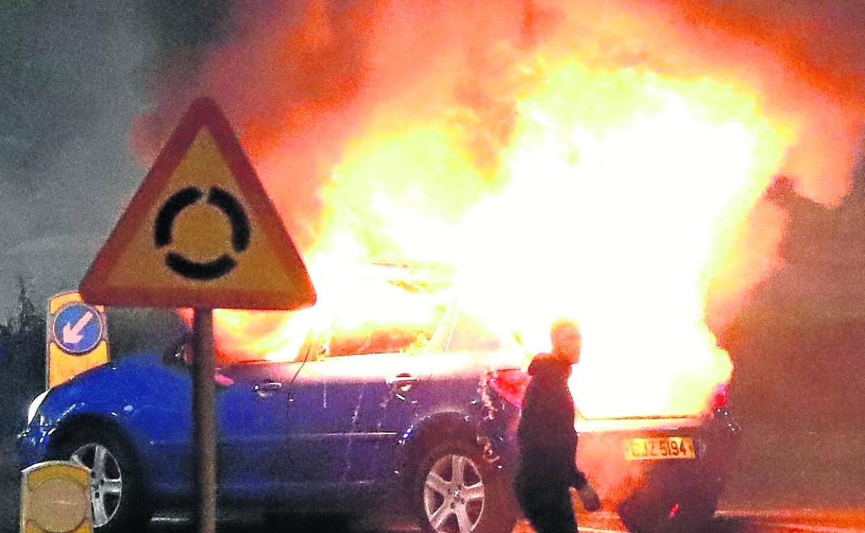 Un hombre pasa junto a un vehículo en llamas durante los disturbios del fin de semana en Ulster.