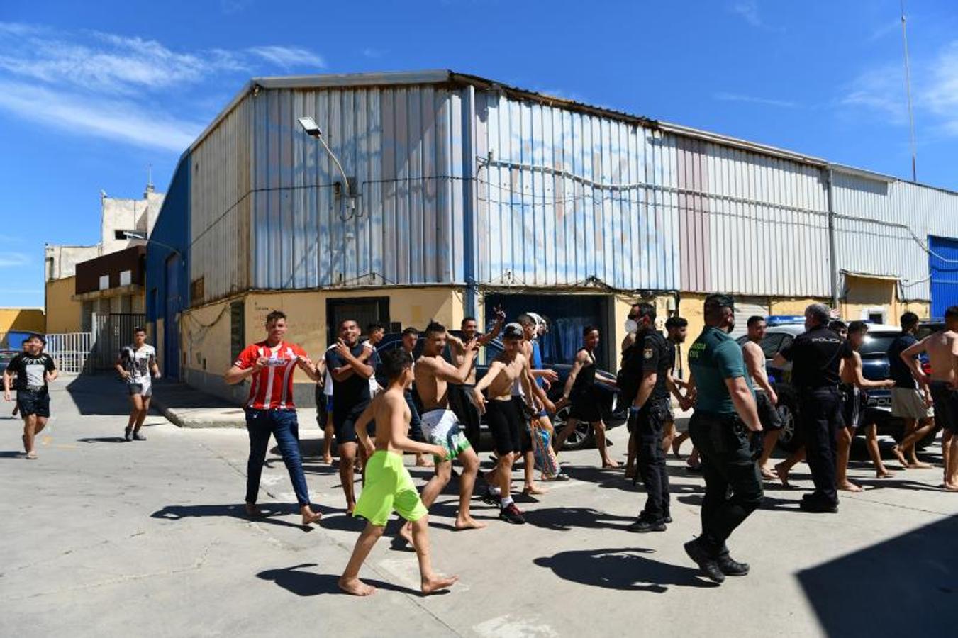 Jóvenes migrantes celebran haber llegado a España mientras las fuerzas de seguridad les trasladan a una nave para alojarlos. 