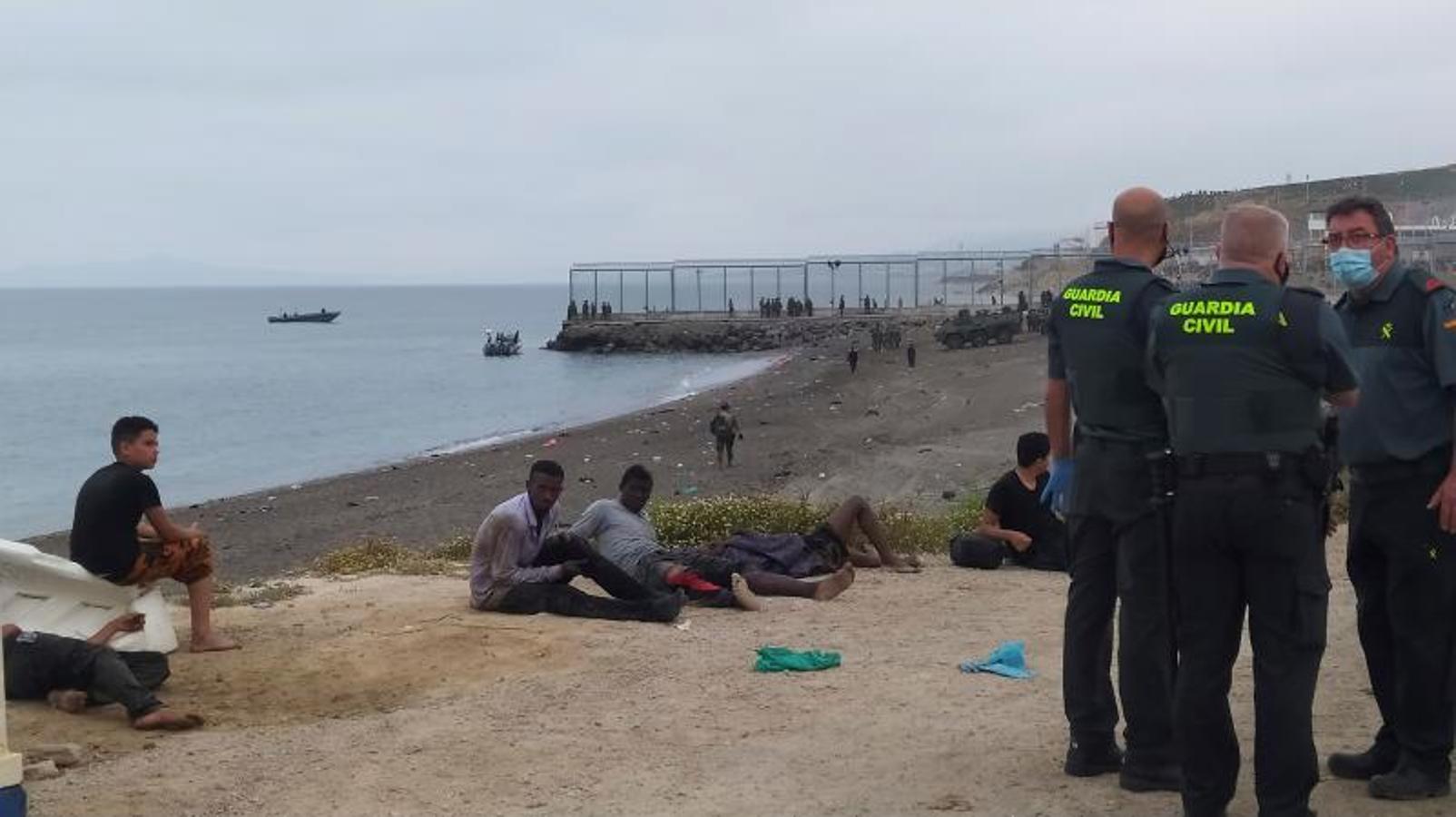 Miembros de la Guardia Civil conversan junto a un grupo de inmigrantes que han cruzado la frontera a nado por los espigones fronterizos de Ceuta. 