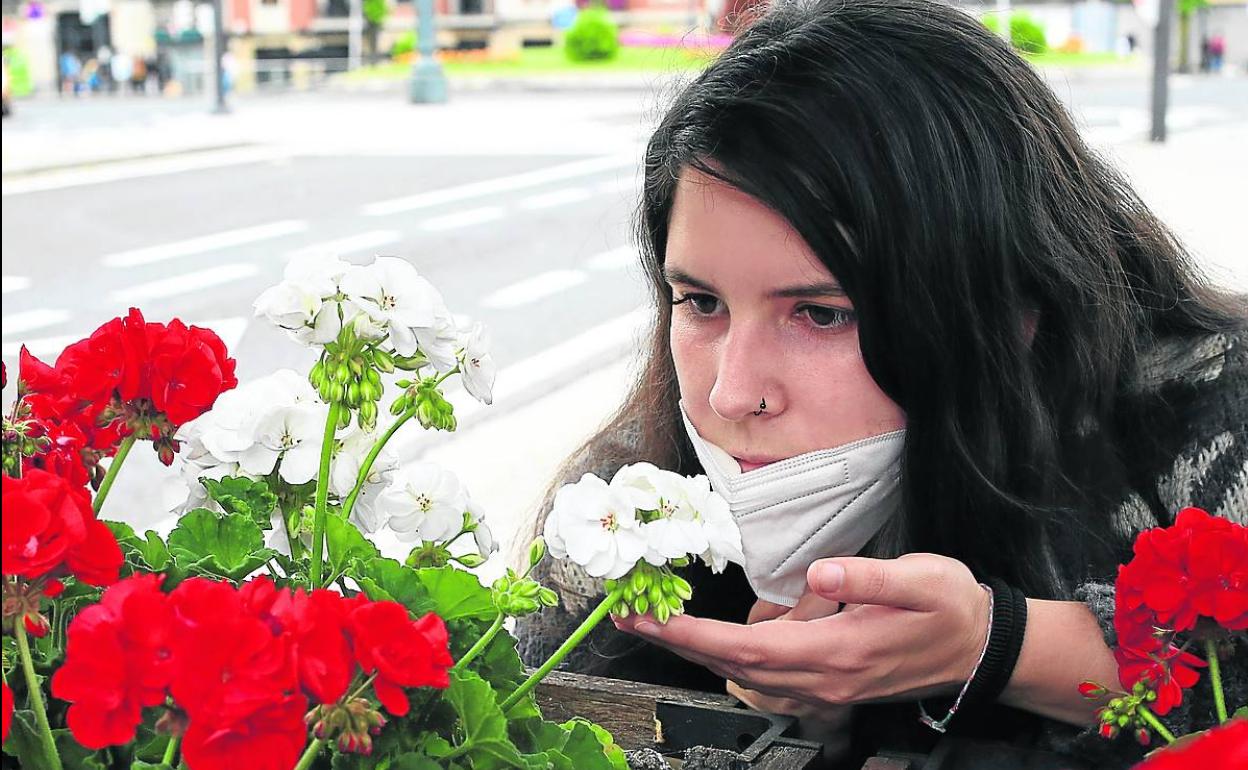 Una joven se retira la mascarilla para oler una flor en un jardín.