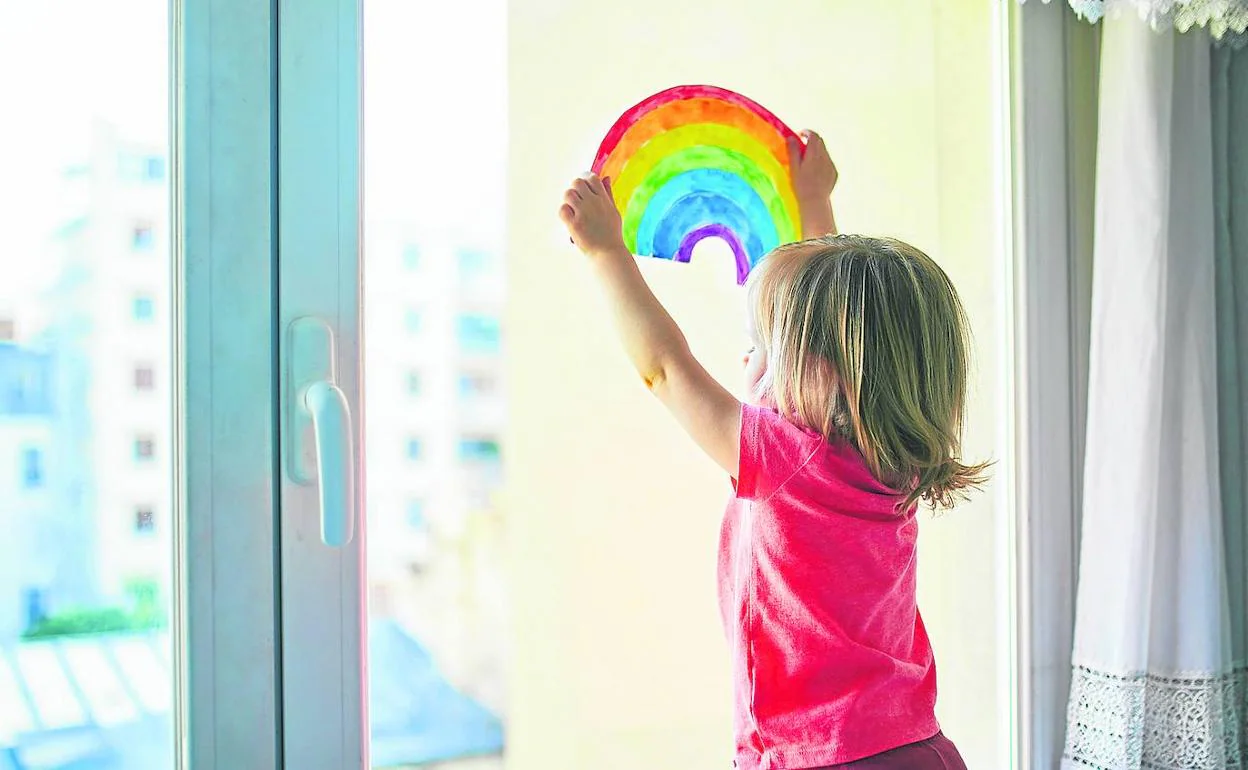 Una niña coloca el dibujo de un arco iris contra el cristal de una ventana. 