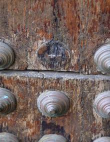 Imagen secundaria 2 - Arriba, capilla del Carmen, con óleos sobre lienzos muy dañados. Sobre estas líneas, huellas del ataque de los xilófagos en uno de los retablos o altares de las cabeceras de las naves laterales, y huecos de los tachones que faltan en la puerta de tea de la basílica. 