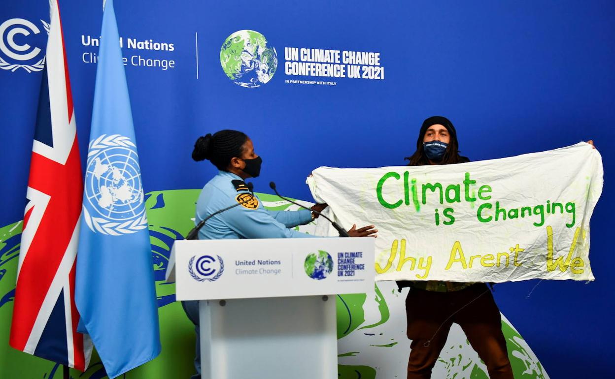 Un activista se cuela en un panel oficial de la COP26 para desplegar un cartel de protesta.