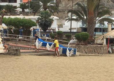 Imagen secundaria 1 - Arriba, un empleado del Golden Beach improvisando unas sillas-hamacas para sus clientes. Abajo, trabajadores retirando de la arena las tumbonas que habían apilado el miércoles, y estampa de los aseos cerrados a cal y canto. 