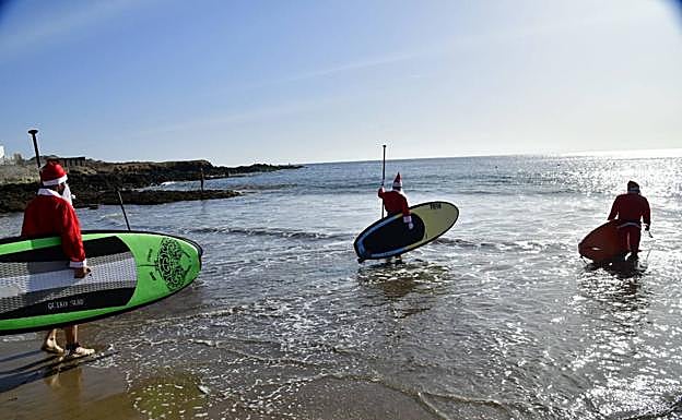 Imagen principal - Papá Noel llega a Arinaga haciendo paddle surf