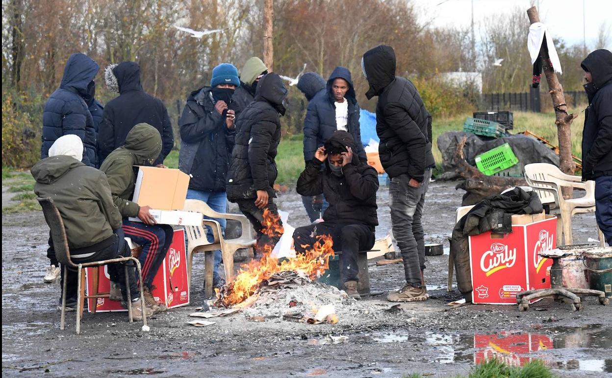Más de una decena de migrantes intentan entrar en calor alrededor de una pequeña hoguera en el Paso de Calais, Francia.