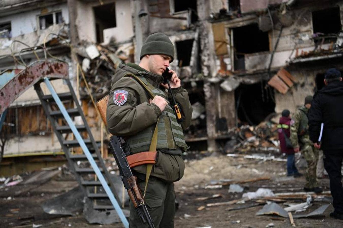 Un militar ucraniano habla por teléfono frente a un edificio destruido.