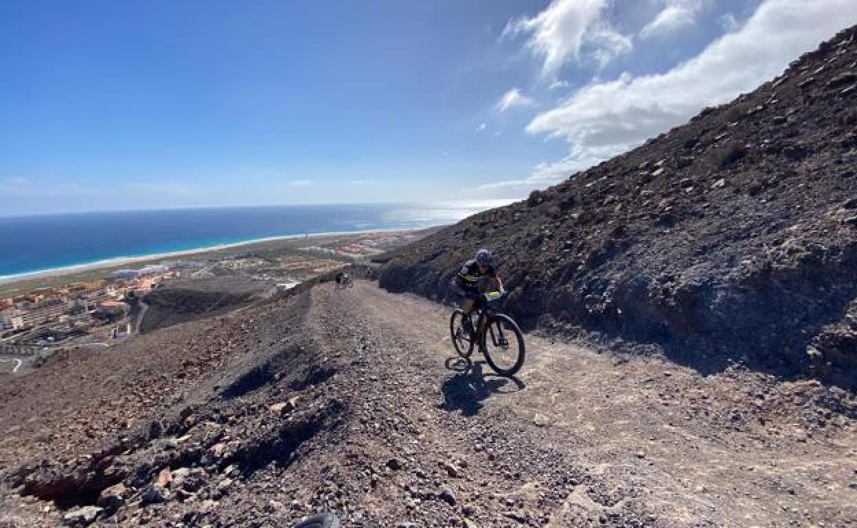 Un ciclista asciende por la montaña con las playas de Jandía al fondo. 