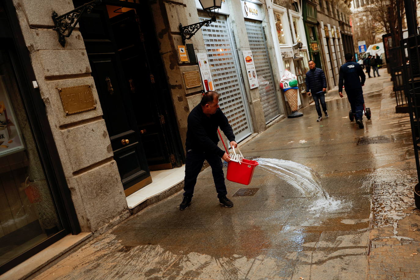 Un hombre limpia la acera delante de un portal en una calle de Madrid. 