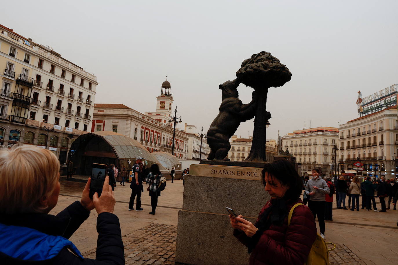 Una persona hace una foto a la estatua del Oso y el Madroño subierto de arena, en la Puerta de Sol de Madrid.