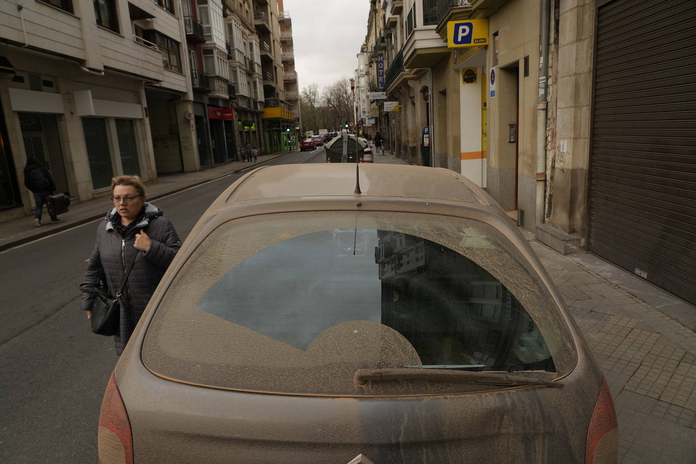 Una mujer pasa junto a un coche cubierto de polvo de barro en Murcia. 